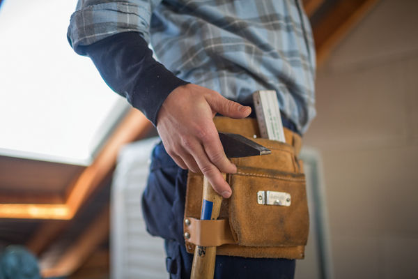 Handwerker greift nach Hammer in seinem Gurt.