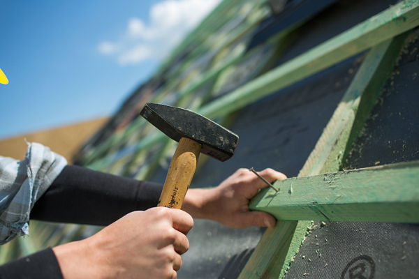 Mann hämmert Nagel in Dachkonstruktion.
