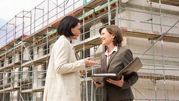 Steuerberaterin und Mandantin unterhalten sich vor einem Haus im Rohbau.