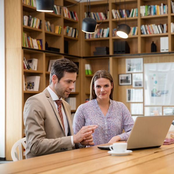 On this picture you can two people sitting in an office in front of a laptop.