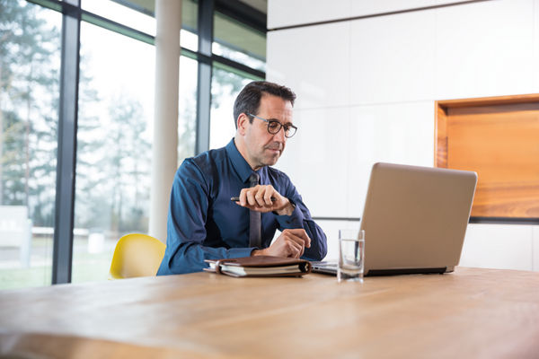 Steuerberater sitzt an Schreibtisch und arbeitet am Laptop.