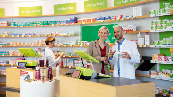 Steuerberaterin und Mandant stehen in einer Apotheke und unterhalten sich.