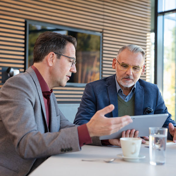 Steuerberater und sein Mandant sitzen im Besprechungsraum und schauen auf ein Tablet-PC