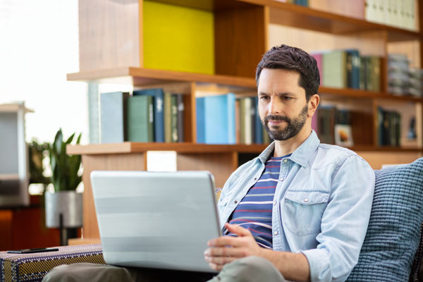 Steuerberater arbeitet an Laptop auf einem Sofa sitzend.