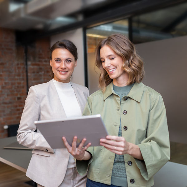 Schmuckbild, Zwei Frauen, eine blickt in die kamera, die andere auf ein Tablet, das sie in der Hand hält
