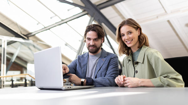 Zwei Unternehmer sitzen nebeneinander und blicken auf Laptop.