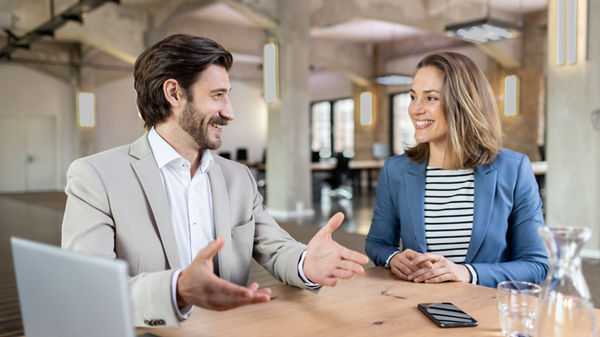 Mann und Frau im Büro am Tisch mit Laptop sprechen miteinander