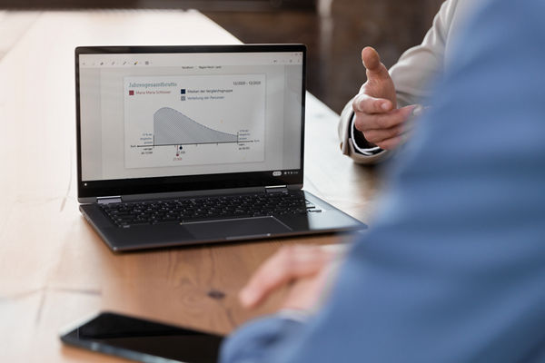 Steuerberater und Mandant sprechen über eine Auswertung, die am Laptop gezeigt wird.