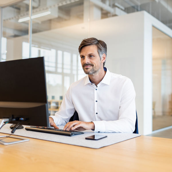 Mann arbeitet an einem Schreibtisch und blickt in PC.