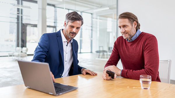 Steuerberater und Mandant sitzen an einem Tisch und blicken gemeinsam auf einen Laptop.