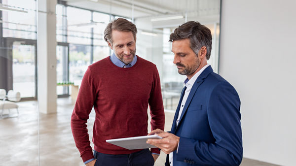 Steuerberater und Mandanten stehen zusammen und blicken auf ein Tablet.