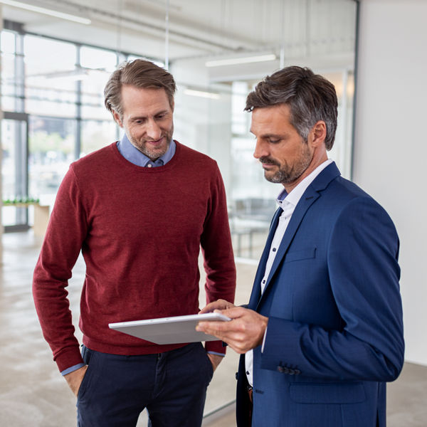 Steuerberater und Mandanten stehen zusammen und blicken auf ein Tablet.