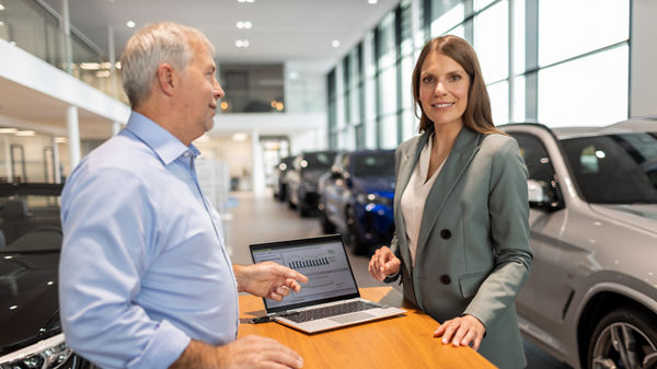 Steuerberaterin und Mandant unterhalten sich in der Verkaufshalle eines Autohändlers.