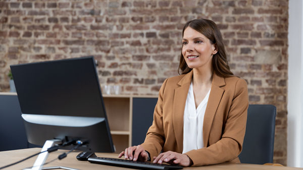 Frau am Schreibtich vor Bildschirm und Tastatur