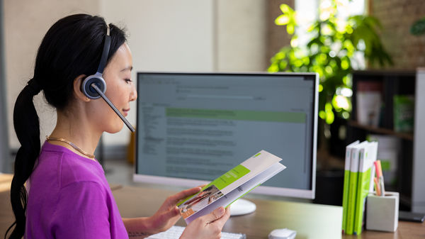 Frau vor dem Monitor im Büro mit Fachliteratur in der Hand