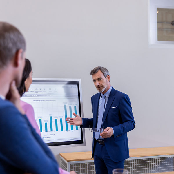 3 Personen stehen vor einem Großbildschirm und sprechen miteinander