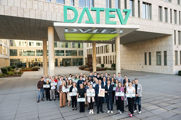 Gruppenfoto von rund 60 Personen vor dem DATEV-Hauptgebäude in Nürnberg. Die Gruppe steht unter dem großen, grünen DATEV-Schriftzug am Eingangsbereich. Viele der Teilnehmenden halten symbolische Spendenschecks in den Händen. Die Stimmung ist freundlich und gemeinschaftlich.
