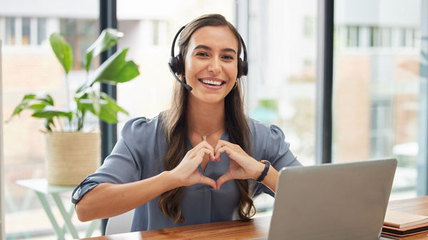 Eine Frau sitzt vor einem Laptop und formt mit ihren Händen ein Herz.