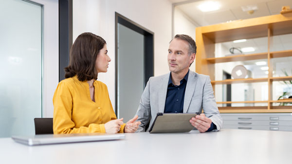 Mann und Frau im Büro am Tisch mit Laptop sprechen miteinander