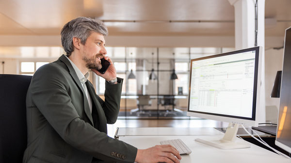 Mann sitzt telefonierend vor Computerbildschirm