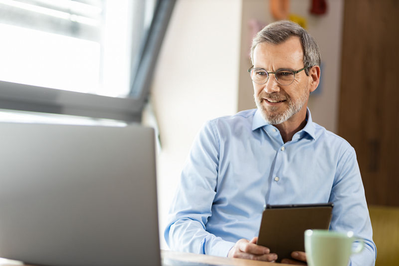 Eine hat ein Tablet in der Hand und schaut gleichzeitig auf einen Laptop-Bildschirm 