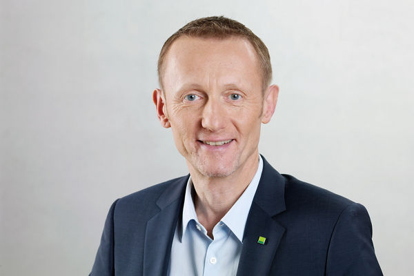 Porträt eines freundlich lächelnden Mannes im blauen Anzug mit hellblauem Hemd. Er hat kurzes hellbraunes Haar und trägt kein Zubehör. Am Revers des Sakkos ist ein kleines grünes DATEV-Logo zu sehen. Der Hintergrund ist neutral und hell.