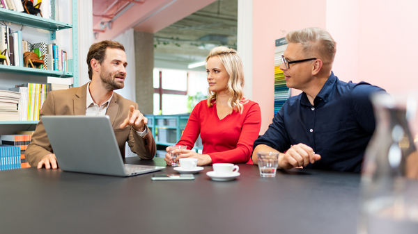 Zwei Männer und eine Frau sitzen im Büro vor dem Laptop