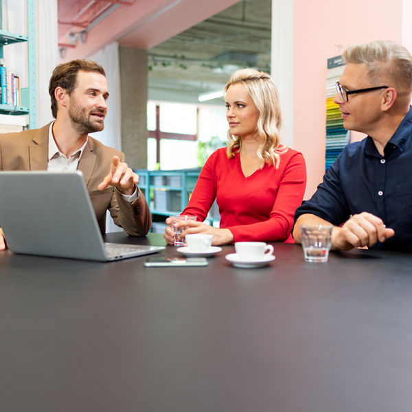 Drei Personen im Gespräch vor dem Laptop