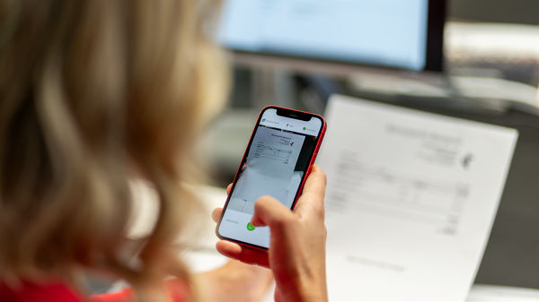 Frau ist im Büro und fotografiert mit dem Handy eine Rechnung ab