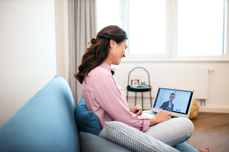 Frau sitzt auf Couch mit Laptop auf ihrem Schoß. 