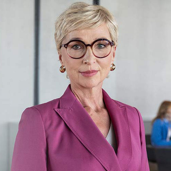 Frau mit lilafarbenem Anzug, im Hintergrund Azubis