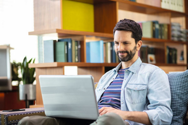 Mann auf Couch mit Laptop auf Knien