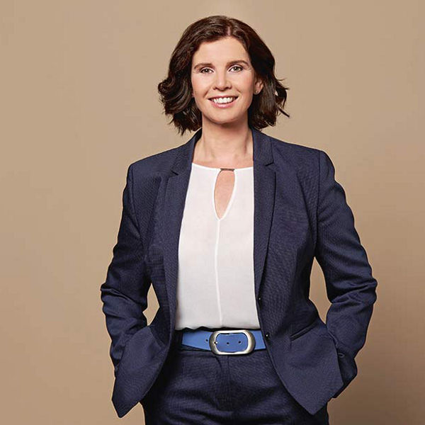 Portrait von Diana Windmeißer, mit schwarzem Sakko und weißer Bluse vor beigem Hintergrund.