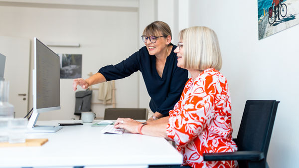 Zwei Damen unterhalten sich und schauen auf einen Monitor.