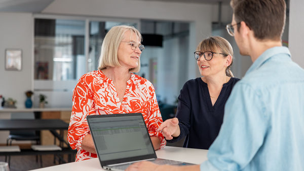 Auf dem Bild sind drei Personen zu erkennen, die in einem Büro zusammen arbeiten. 