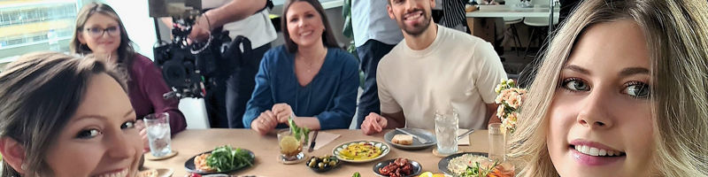 Mitarbeitende der DATEV sitzen nach dem Fotoshooting gemeinsam an einem gedeckten Tisch und lächeln in die Kamera.