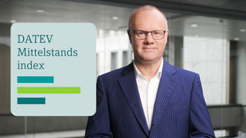 Ein Mann im dunkelblauen Nadelstreifenanzug mit weißem Hemd und Brille steht vor einer modernen Glasfassade. Links im Bild befindet sich eine Grafik mit dem Titel ‚DATEV Mittelstandsindex‘ sowie drei unterschiedlich langen horizontalen Balken in Blau- und Grüntönen.