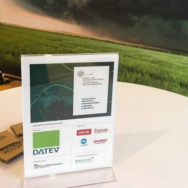 Tischaufsteller mit Logos verschiedener Partner, darunter DATEV, vor einem Wandbild mit einer dramatischen Sturmwolke über grüner Landschaft.