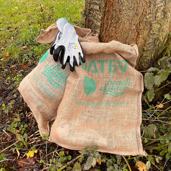 Zwei Jutesäcke mit grünem DATEV-Aufdruck lehnen an einem Baum; darauf liegt ein Paar Arbeitshandschuhe.