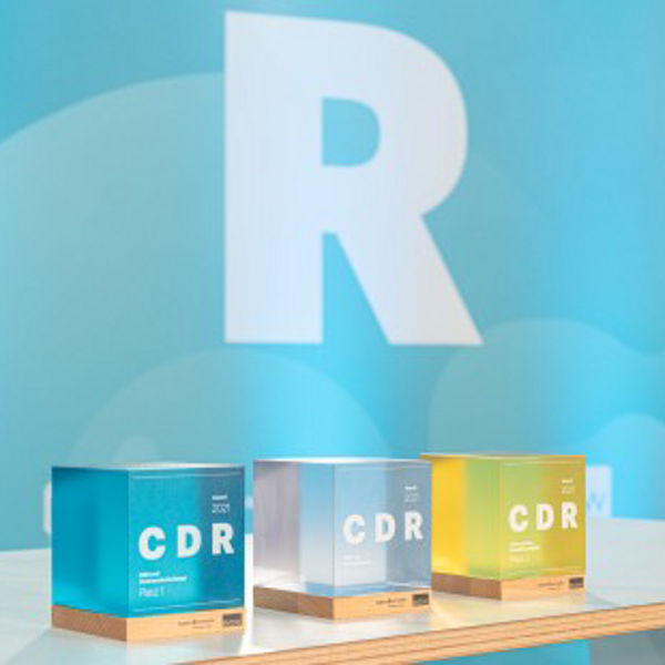 Drei bunte Würfel mit der Aufschrift ‚CDR‘ stehen nebeneinander auf einem Tisch, im Hintergrund eine große hellblaue Wand mit dem Buchstaben R.