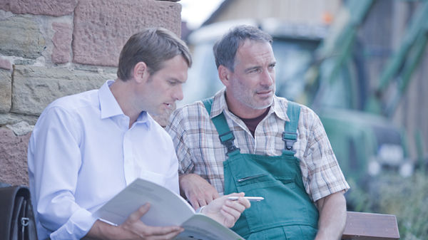 Steuerberater und sein Mandant sitzen auf einer Bank beim Mandanten im Landwirtschaftsbetrieb