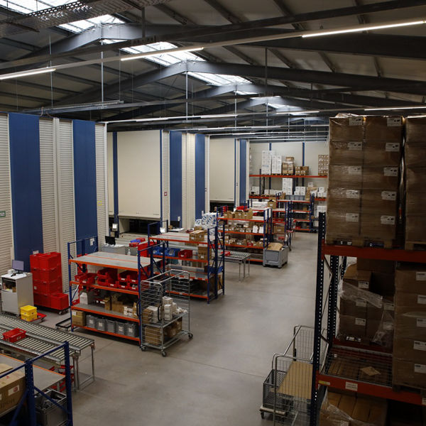 Innenaufnahme eines modernen Lagers mit Hochregalen, Fördertechnik und zahlreichen beschrifteten Kartons. Die Halle ist gut ausgeleuchtet, organisiert und wirkt effizient strukturiert.