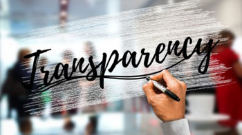 Eine Hand schreibt mit schwarzem Stift das Wort &#39;Transparency&#39; auf eine halbtransparente Fläche vor verschwommenen Personen in einem Büro.